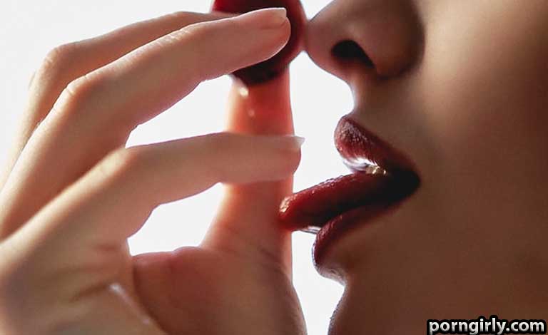 Close-up of a person's lips near a finger holding a cherry between them.